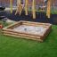 Sandkasten aus Holz mit Sand und Spielzeug im Garten bei einem Spielplatz.