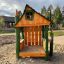 Nills Spielhaus aus Holz auf einem Spielplatz mit Sandboden und grünen Holzelementen.