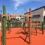 Spillikins Klettergerüst aus Holz mit Schaukel und Kletterelementen auf Spielplatz mit orangem Boden
