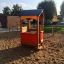 Spielhaus aus Holz mit rotem Verkleidung auf Sandspielplatz.