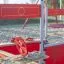Rotes Jupiter Sandkasten Spielgerät mit Spielsteuerrad und Sitzbank im Sand auf dem Kinderspielplatz