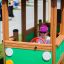 Kind spielt in Bus Spielhaus Kinderspielhaus aus Holz mit grünem Design und rotem Lenkrad