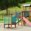 Epsilon Barrierefreie Spielplatz mit Rutsche, Klettergerüst und Brücke aus Holz und Metall.
