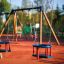 Holzbabyschaukel mit Holzrahmen und blauen Sitzflächen auf einem Spielplatz.