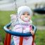 Holzbabyschaukel mit Baby in Herbstkleidung, auf Spielplatz hängend.