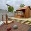 Spielhaus mit Zaun und Matschtisch aus Holz auf kinderspielplatz mit kleiner Rutsche und Bodenbelag 