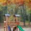 Knirps II Spielturm mit grünem Rutschbahn und Kletterwand im herbstlichen Waldspielplatz