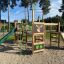 Wald - Spielturm - Klettergerüst mit Rutsche aus Holz und grünen Akzenten auf einem Spielplatz.