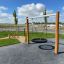 Nestschaukel Robinie (BNS 90 cm) aus Holz mit runder Netzschaukel auf Spielplatz bei blauem Himmel.