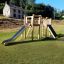 Alstad Spielkombination mit Rutsche aus Holz auf Spielplatz bei Sonnenschein