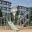 Kinderspielplatz mit Alpha Centauri Klettergerüst und Rutsche vor Wohnhäusern.