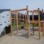 Aztek Spielanlage mit Kletterwand und Rutsche aus Holz und Metall auf einem Sandspielplatz.