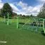 Balancier Spielplatz Netz auf grünem Spielplatz mit blauem Himmel und Bäumen im Hintergrund.