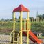 Grashüpfer Spielturm mit roter Rutschbahn und Kletterelementen auf Sandspielplatz