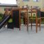 Kinderspielplatz mit Wetpour 60 Sicherheitsboden und Holzspielgeräten mit Rutsche und Kletterwand.