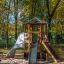 Spielturm mit Kletterwand und Rutsche im Waldspielplatz aus Holz.