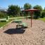 Umbrela roter Sonnenschutz auf einem Spielplatz mit Sandboden.