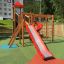 Twister Spielanlage mit Rutsche aus Holz und rotem Kunststoff auf Spielplatz mit grünem Bodenbelag.