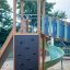 Twister Spielanlage mit Rutsche aus Holz mit Kletterwand und grüner Rutsche auf Sandplatz