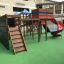 Weltraumstation mit Spieltürme und Spiralrutsche auf grünem Spielplatz mit Kletterwand und Netz.