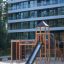 Spieltürme mit Tunnel, Kletterwand und Rutsche auf Sandspielplatz vor modernem Gebäude